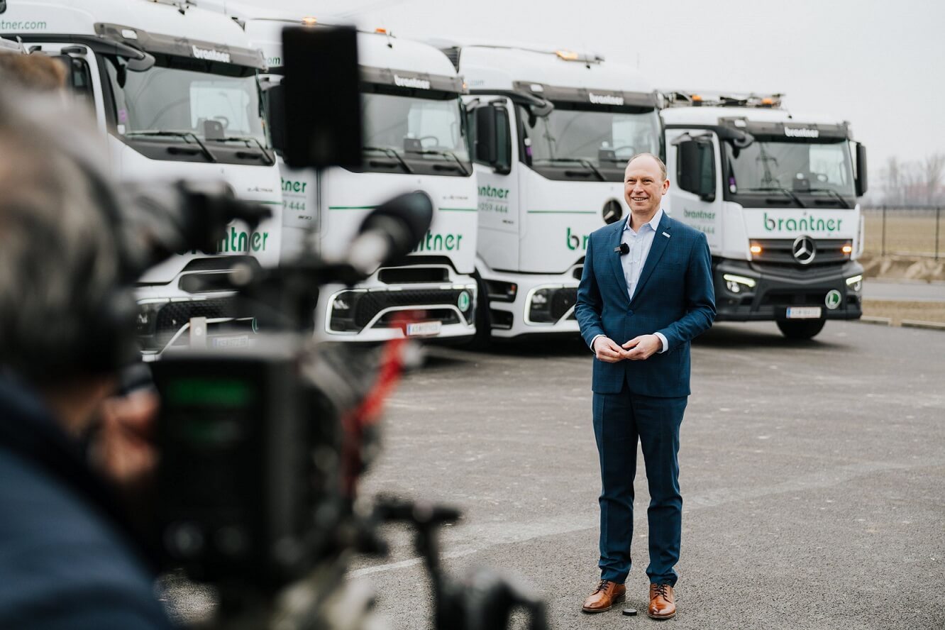 Ein Mann wird gefilmt und im Hintergrund die E-LKW-Flotte von Brantner